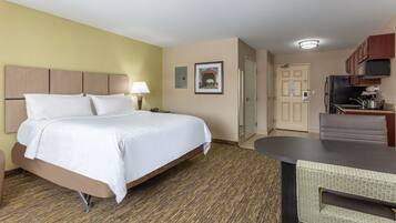 A hotel room with a bed, a desk, a chair, a kitchenette, and a door.