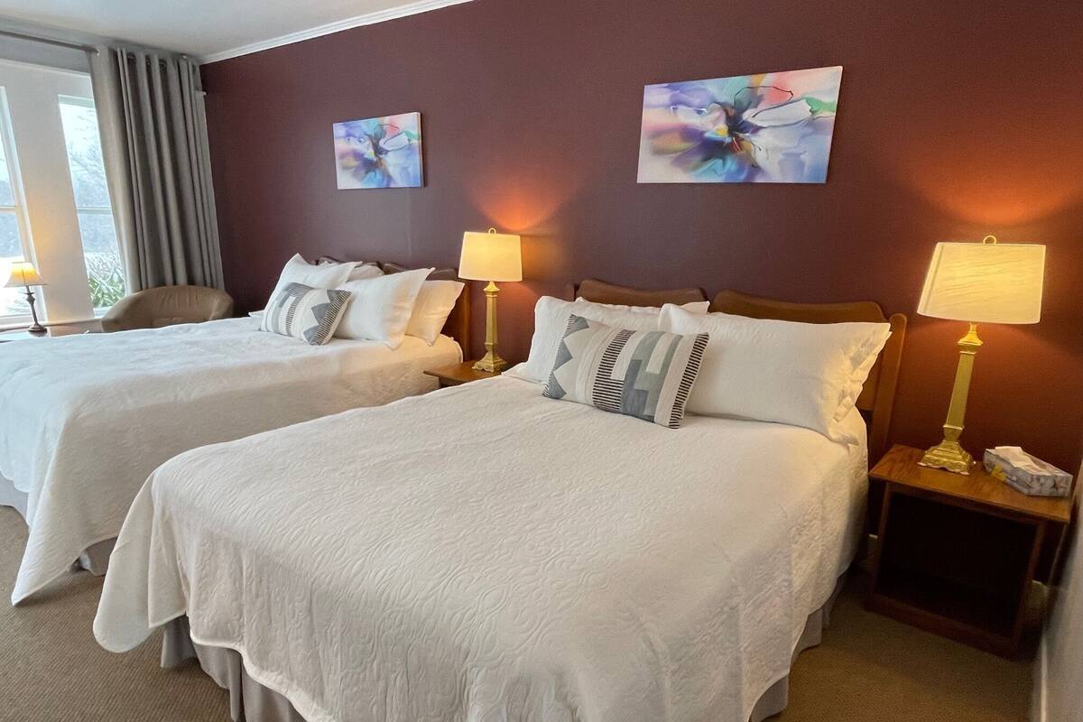 Habitación de hotel con dos camas, cada una con una almohada y una lámpara de noche. Hay pinturas abstractas en las paredes.