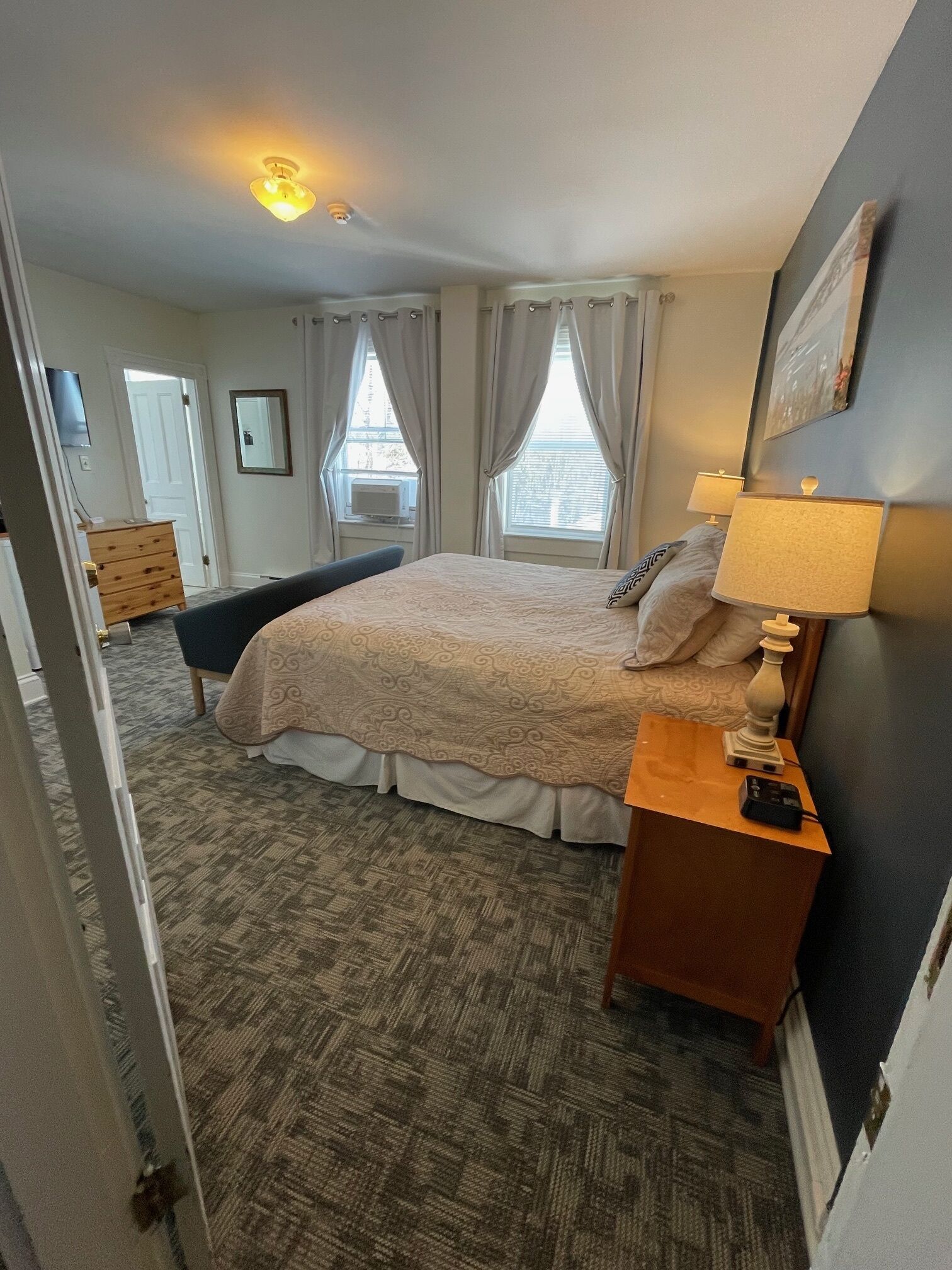 Une chambre à coucher avec un lit, des lampes de chevet, une commode, un miroir et une fenêtre avec des rideaux.