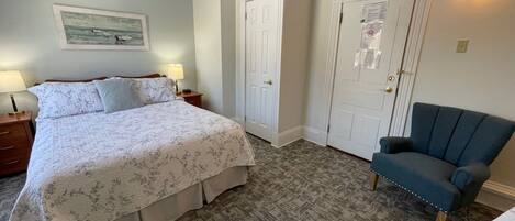 A bedroom with a bed, two bedside tables with lamps, a chair, and a door with a light switch.