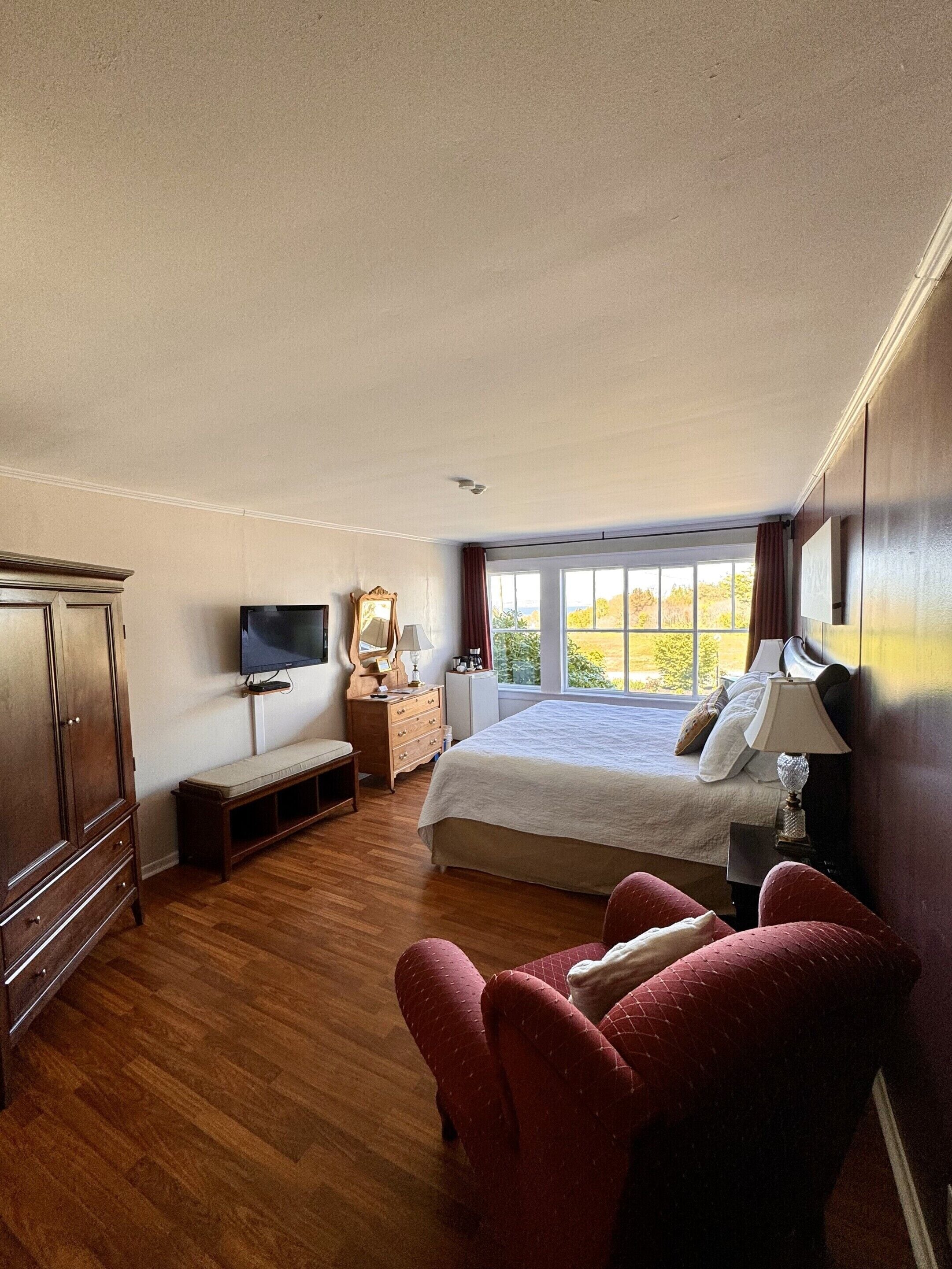 A bedroom with a bed, a TV, a bench, a chair, and a dresser.