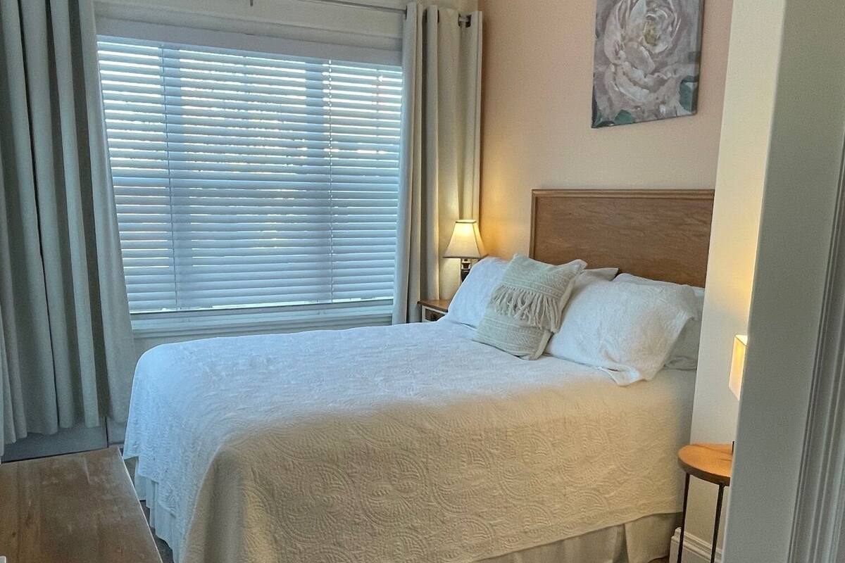 Un dormitorio ordenado con cama, mesita de noche, lámpara y un cuadro en la pared.