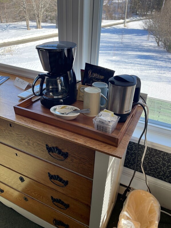 Una encimera de madera con una cafetera, tazas, un hervidor y una bandeja con cuchara y sobres de azúcar.