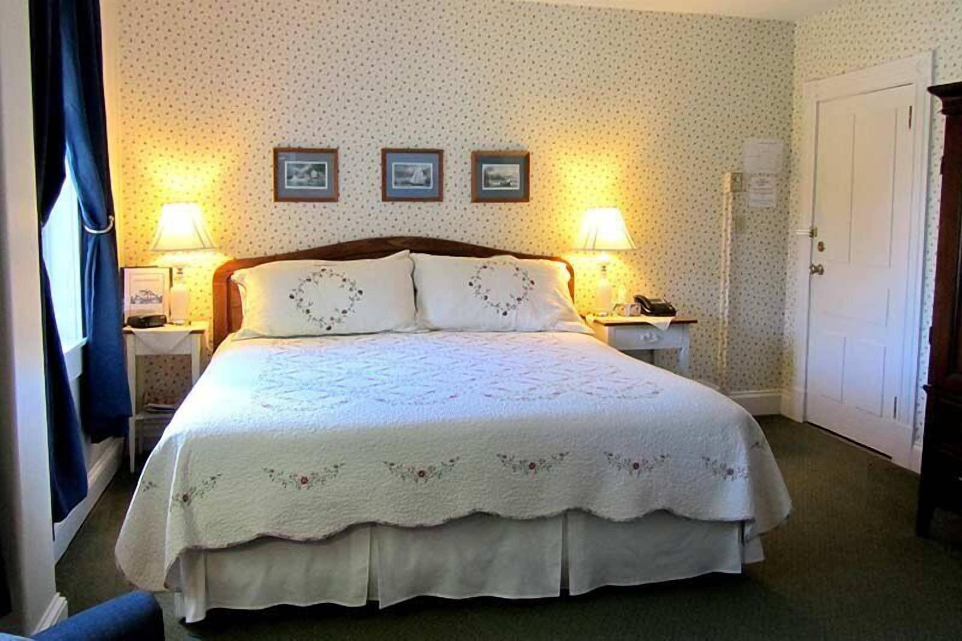 A neatly made bed with a white quilt, two bedside lamps, and three framed pictures on the wall.