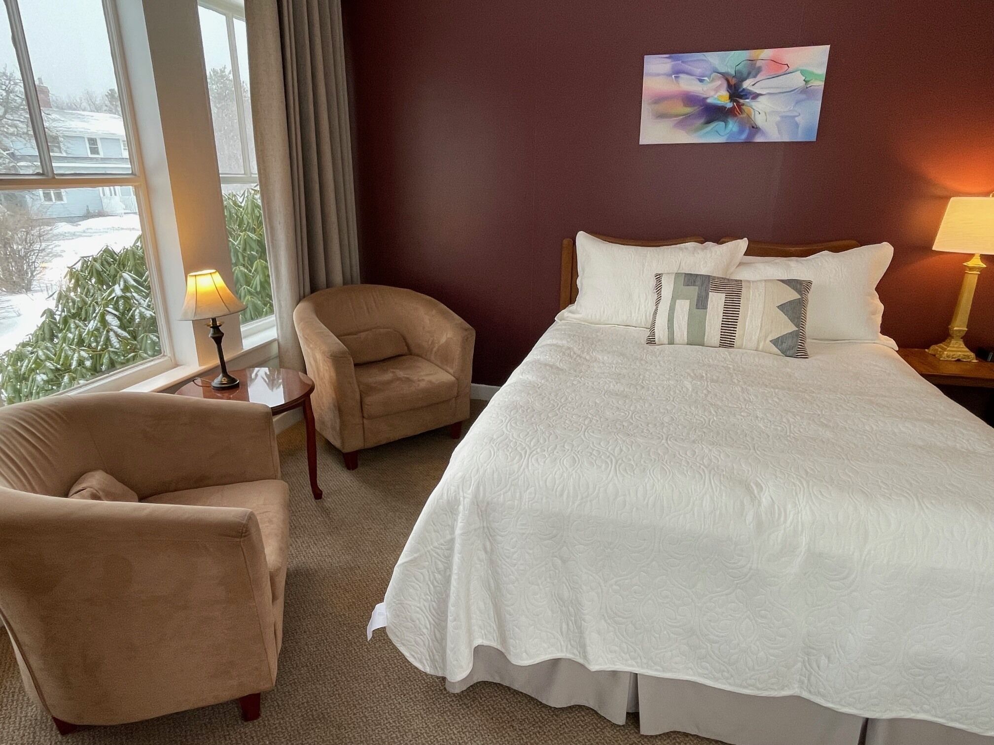 A hotel room with a bed, two armchairs, a lamp, and a painting on the wall.