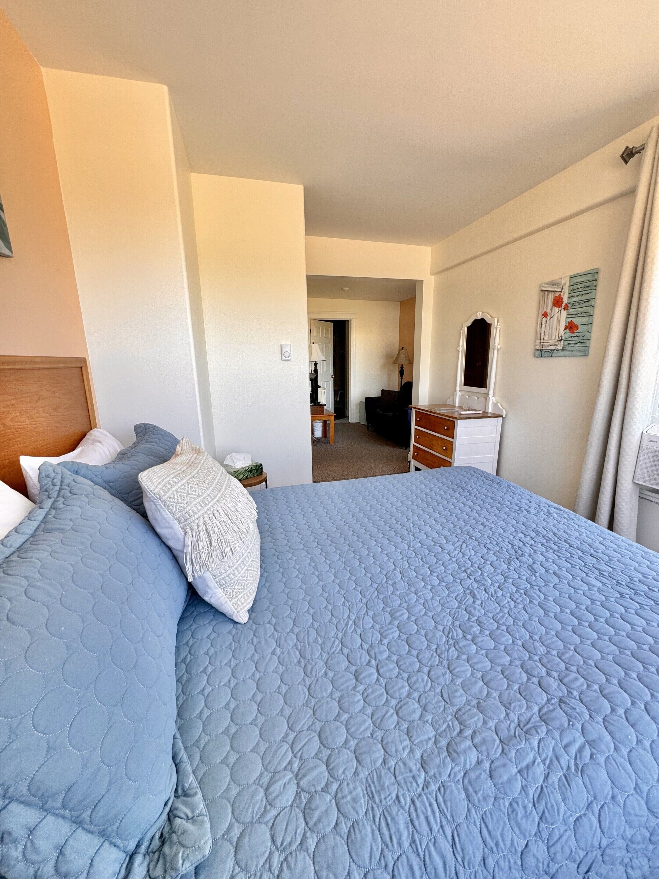 Een hotelkamer met een groot bed, een dressoir, een spiegel en een deur naar een andere kamer.