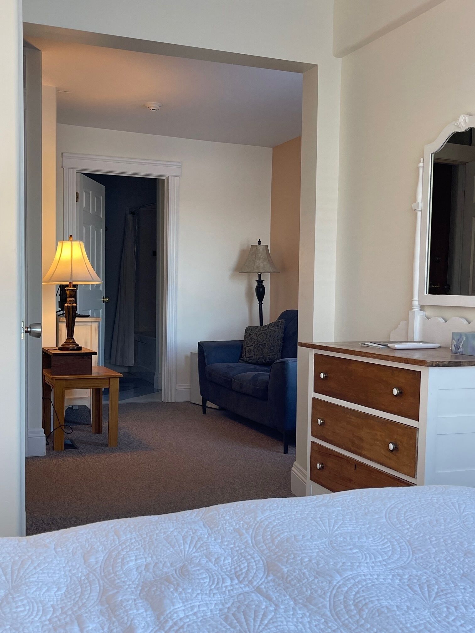 A hotel room with a bed, a desk with a lamp, a sofa, and a dresser.