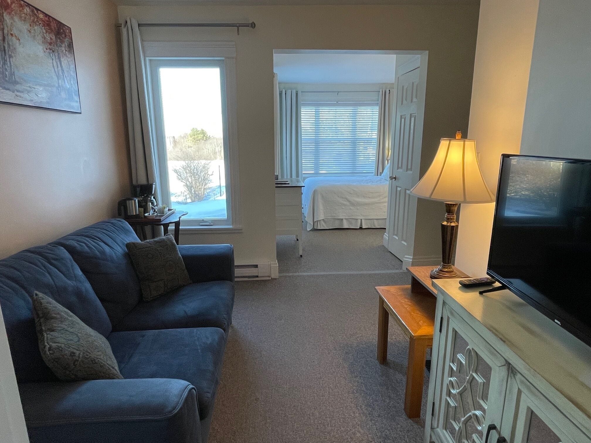 A living room with a sofa, a television, a lamp, and a bed in the background.