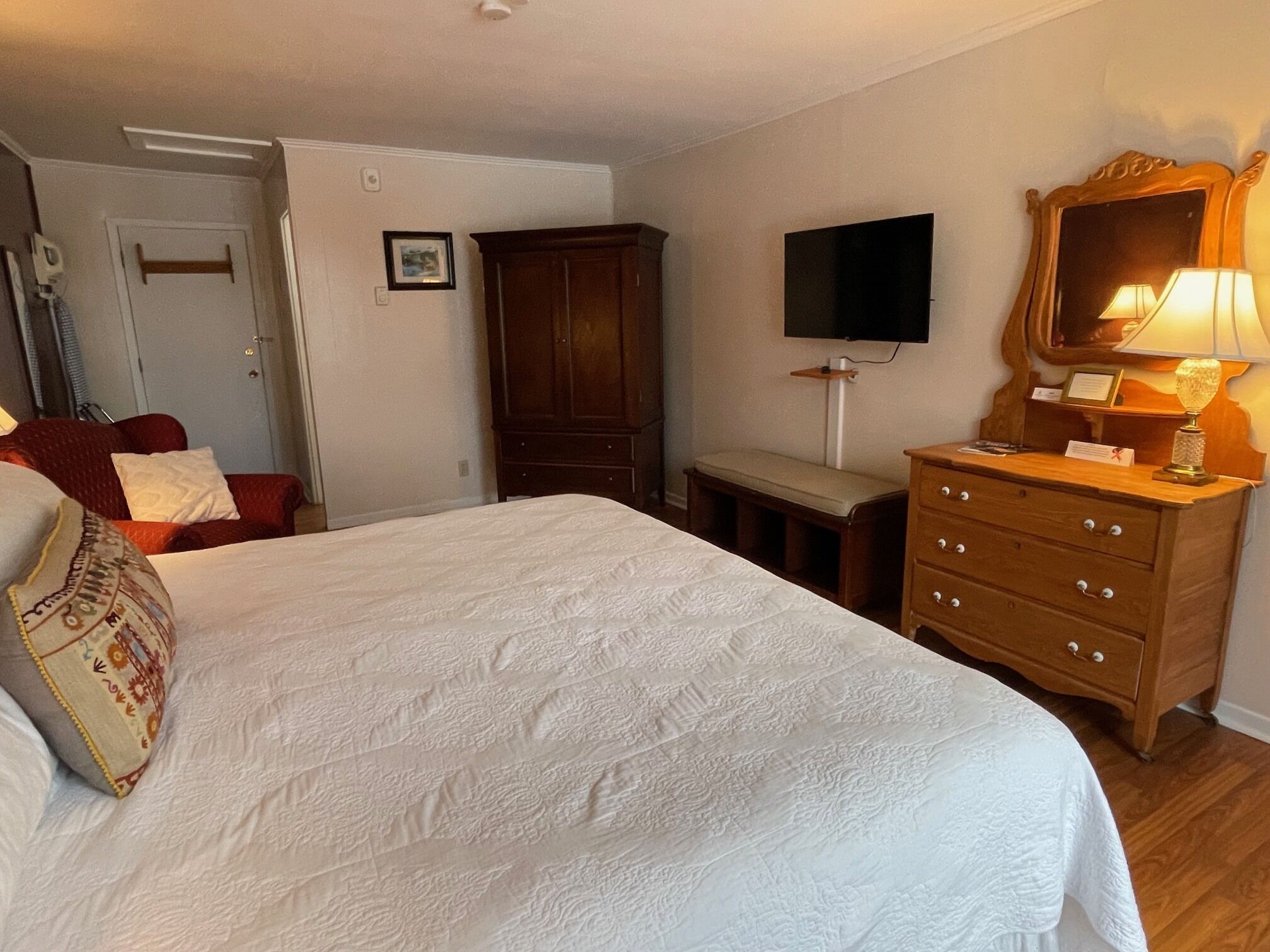 A bedroom with a large bed, a wooden dresser, a television, and a mirror.