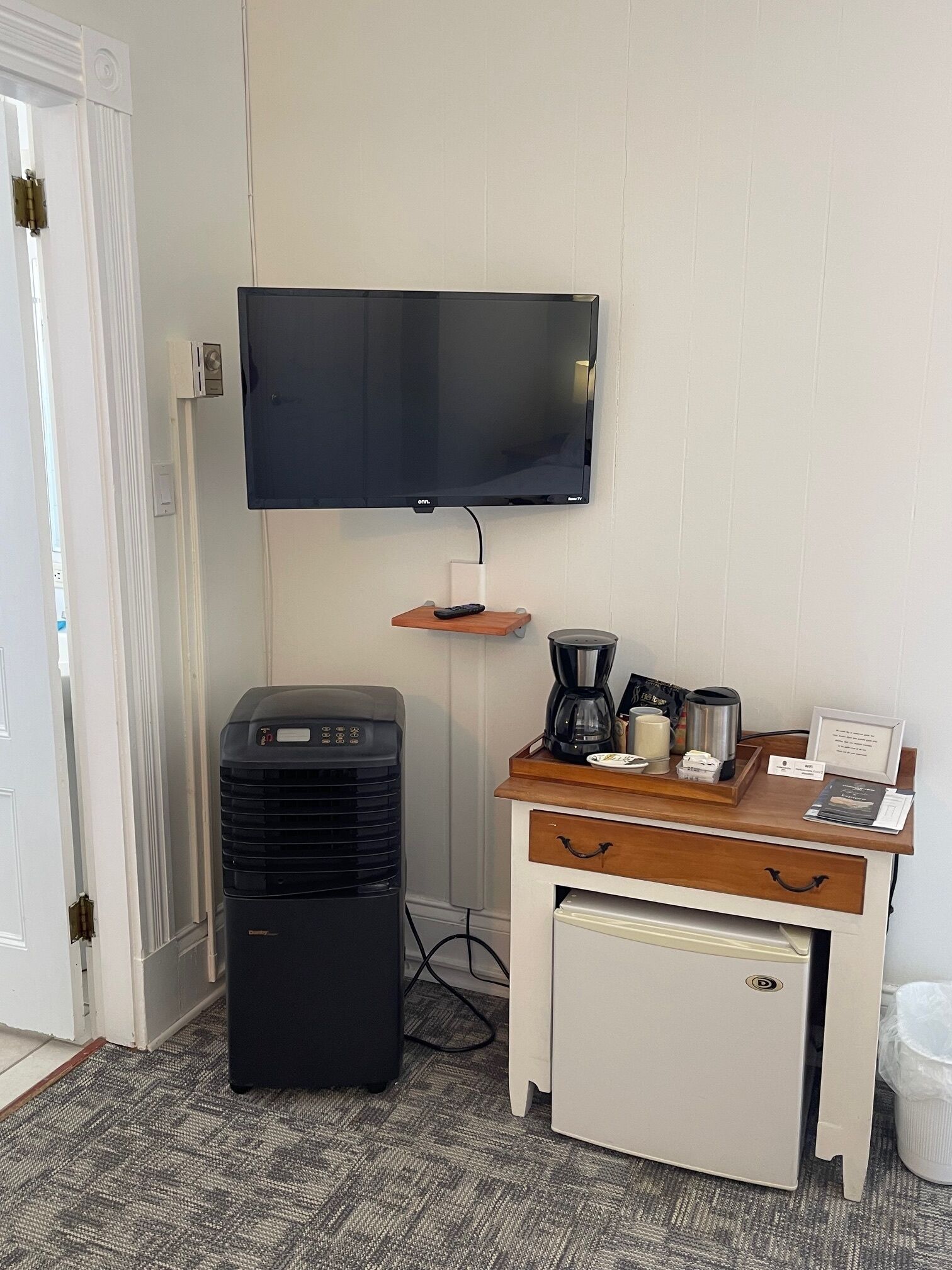Ein Hotelzimmer mit Flachbildfernseher, Minikühlschrank, Kaffeemaschine und einem kleinen Schreibtisch mit Schubladen.