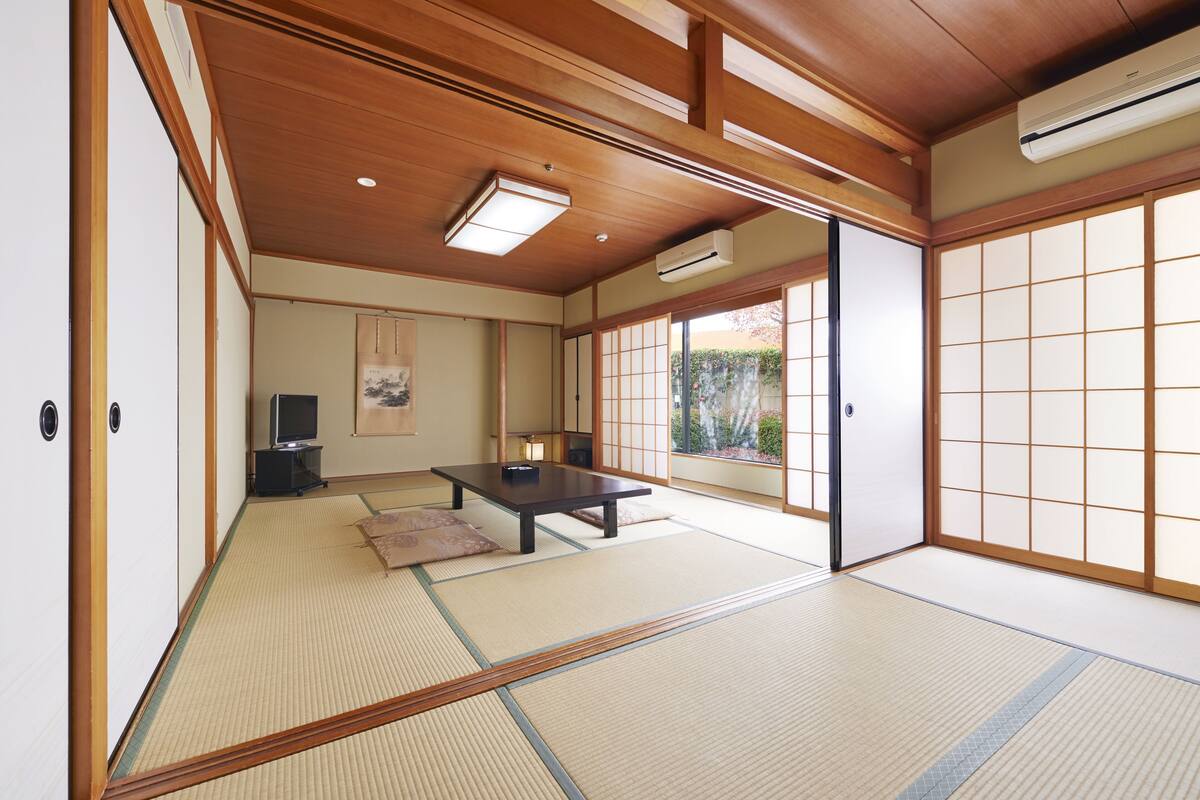 Una habitación japonesa tradicional con suelo de tatami, una mesa baja, un televisor y puertas correderas.