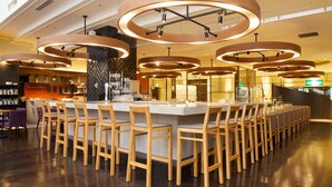 Zona de bar moderna con una barra alargada, múltiples sillas de madera y focos circulares en el techo.