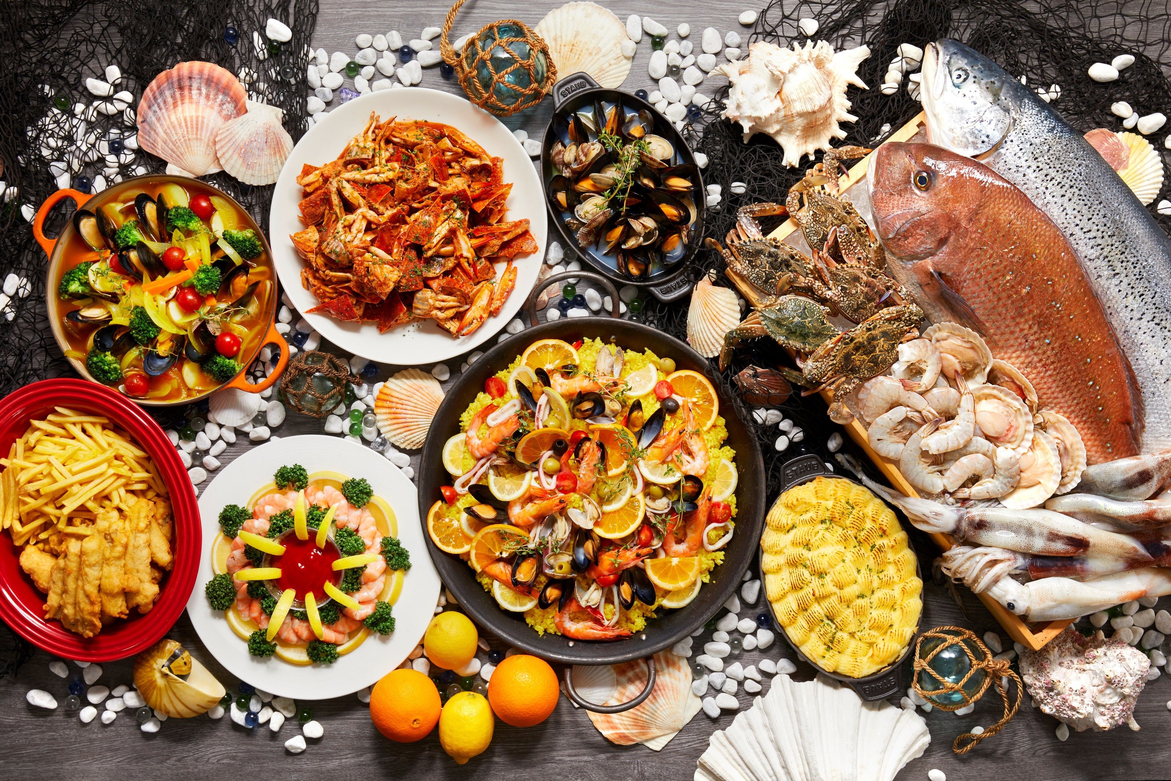 Une variété de plats de fruits de mer, notamment des moules, des crevettes et du poisson, présentés sur une table en bois, entourée de coquillages et d’autres éléments décoratifs sur le thème des produits de la mer.