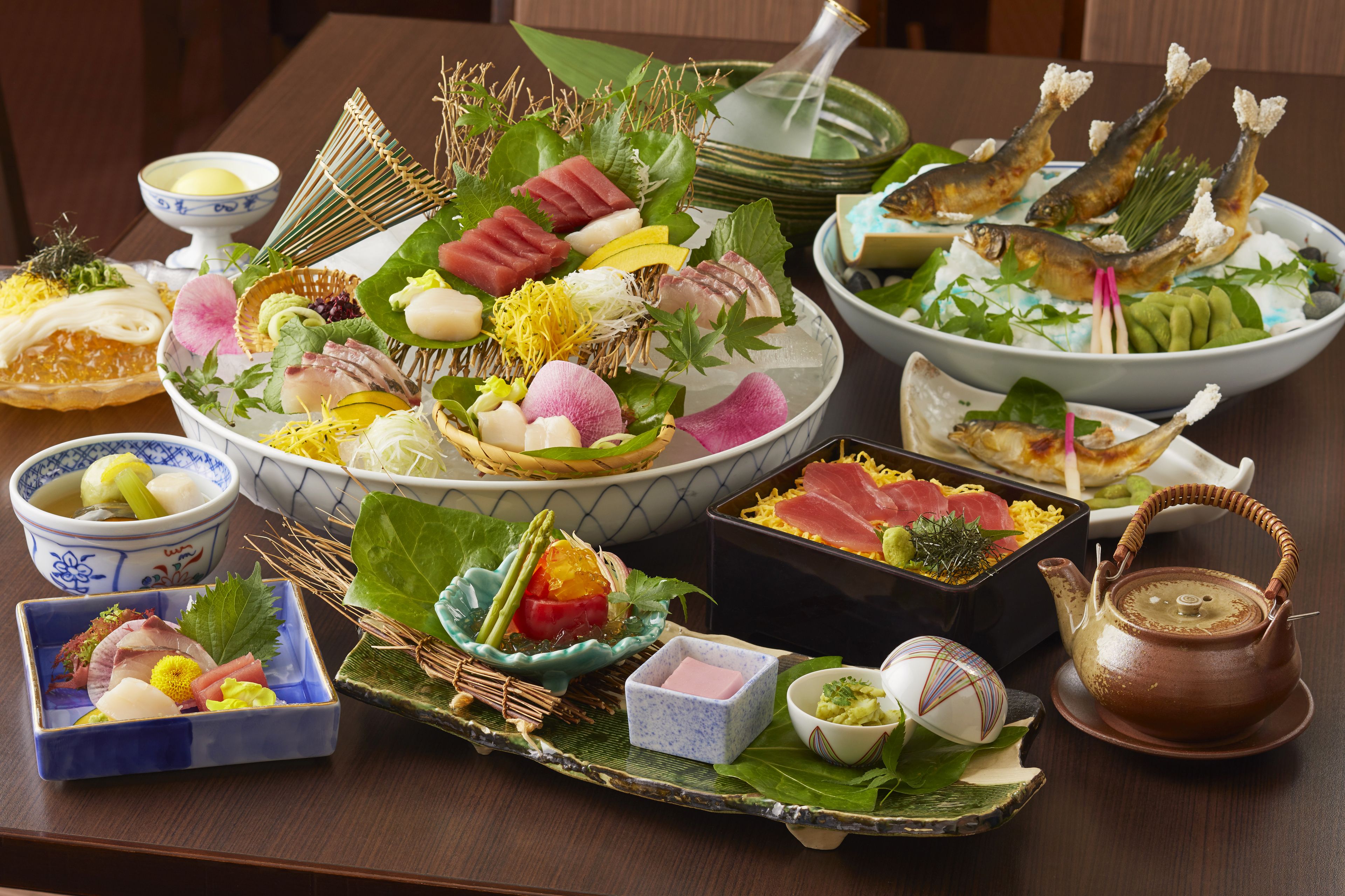A variety of Japanese dishes arranged on a table, including sashimi, vegetables, and a teapot.