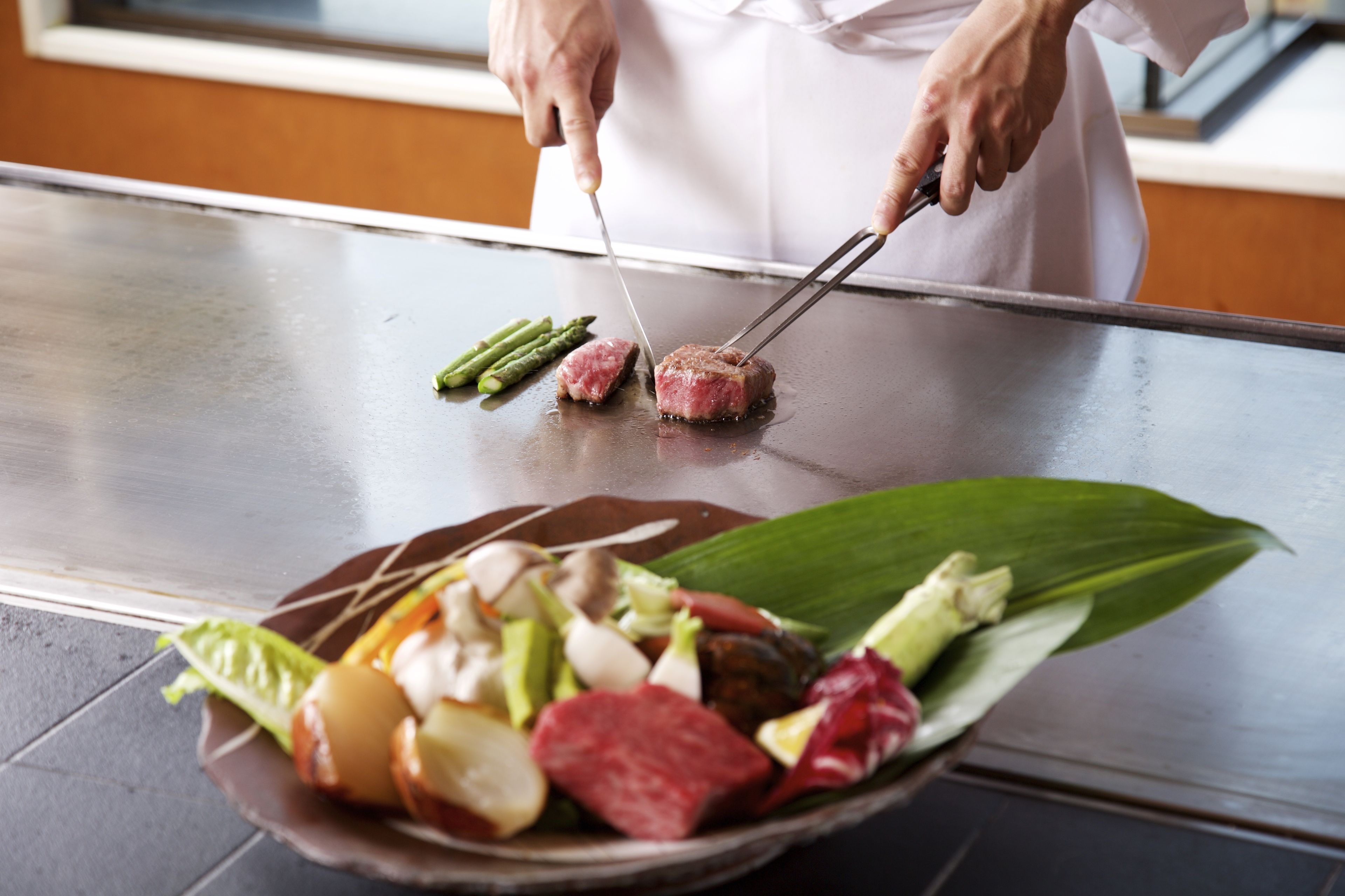 Un cocinero preparando comida en una plancha con diversos tipos de carne y verduras.