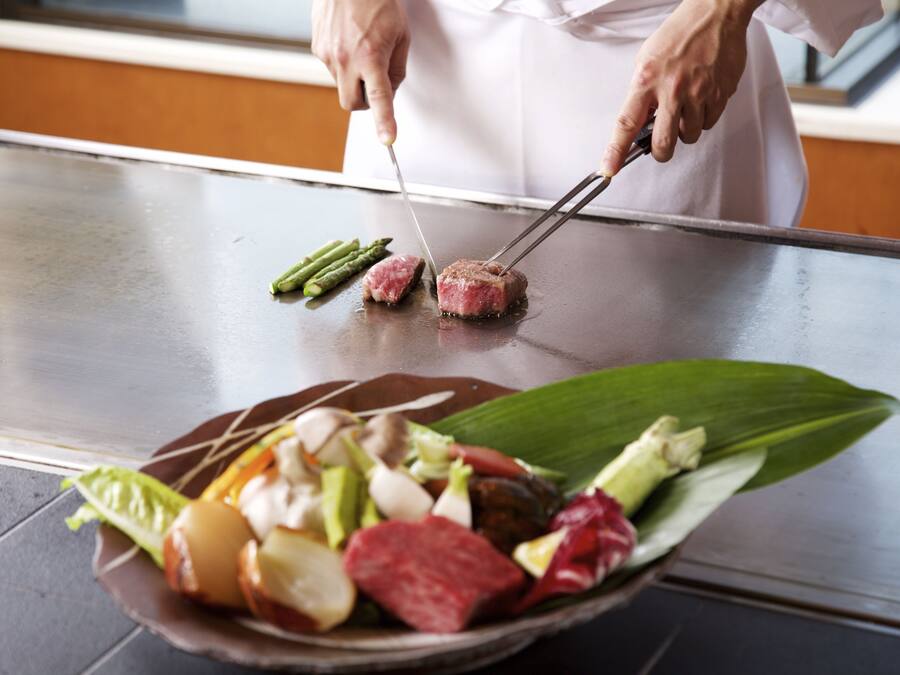 Un cocinero preparando comida en una plancha con diversos tipos de carne y verduras.