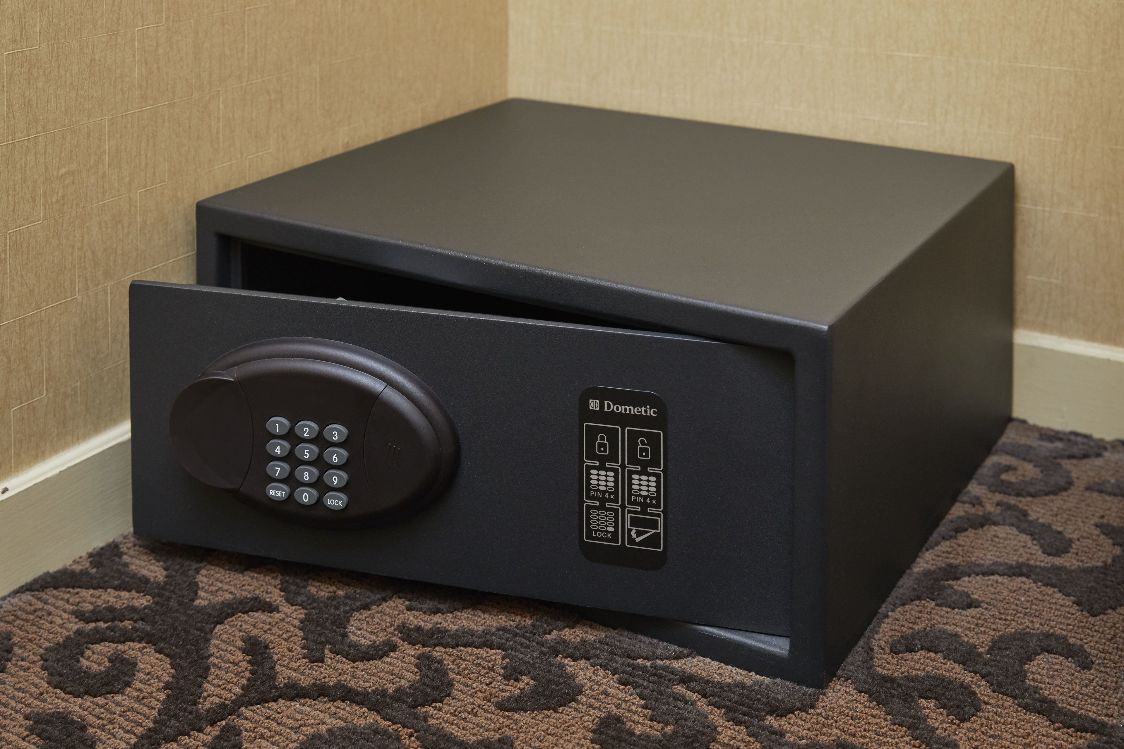 A black safe with a keypad and a lock symbol, placed on a patterned carpet.