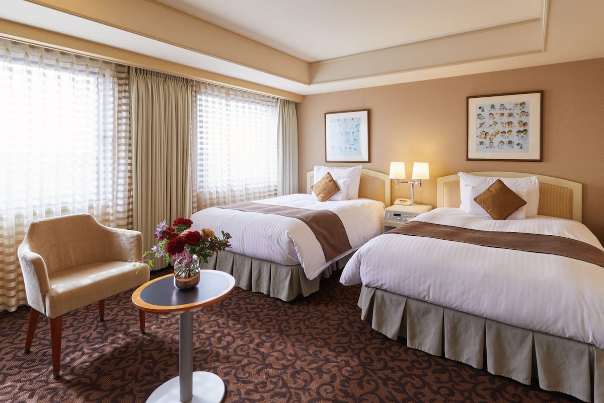 Una habitación de hotel con dos camas, una silla, una mesita y un florero con flores.