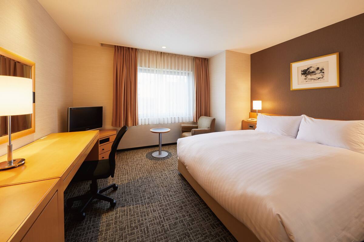 Una habitación de hotel con cama, escritorio, silla, televisor y una mesita.
