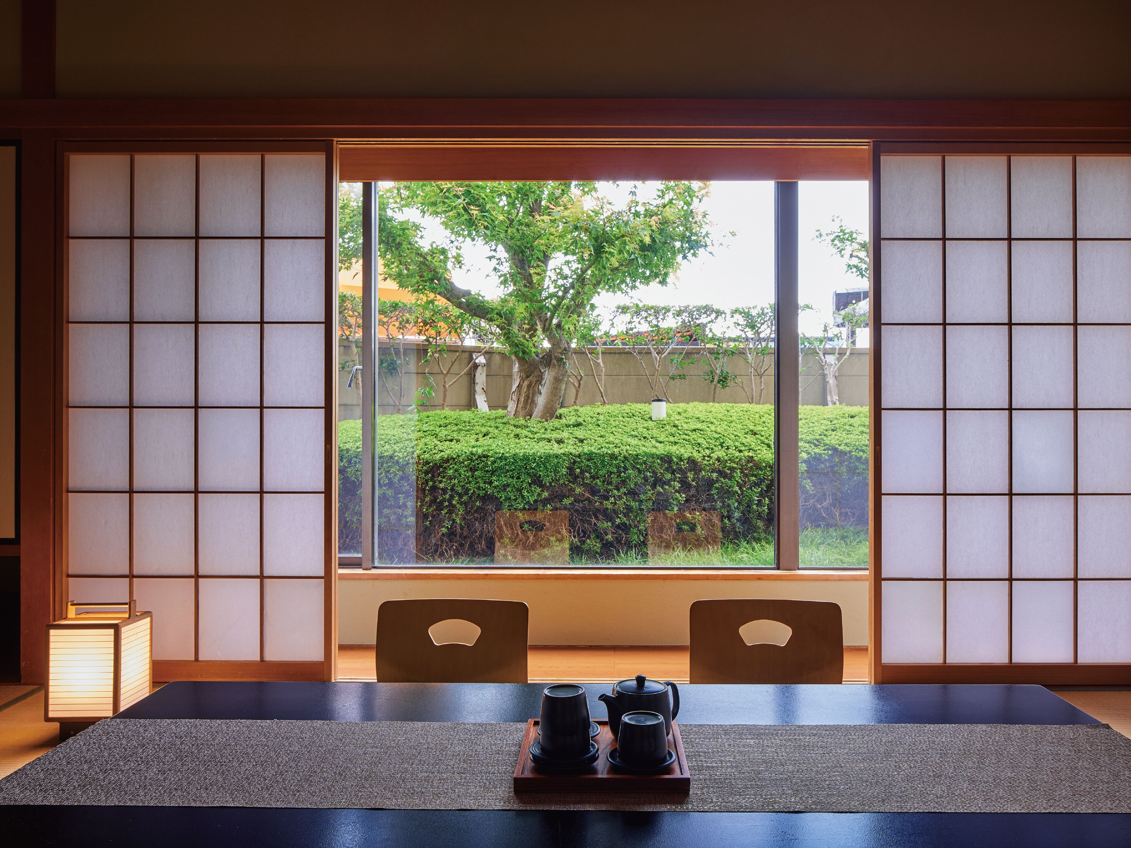 Perinteinen japanilainen huone, jossa on tatamimatto, matala pöytä, kaksi tuolia ja liukuva shoji-seinä.