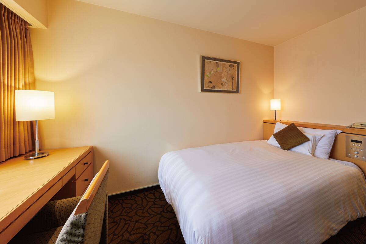 Una habitación de hotel con cama, mesita de noche, lámpara y un cuadro en la pared.