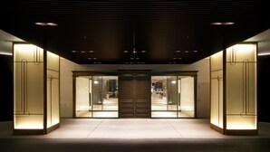 Entrada de hotel con diseño moderno, destacando una puerta central flanqueada por puertas de vidrio y paneles iluminados.