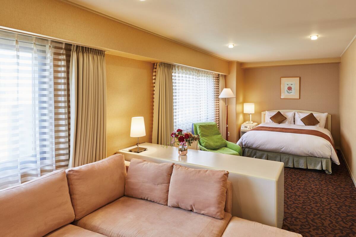 Habitación de hotel con sofá, escritorio, silla verde, cama con almohadas, lámpara y un cuadro en la pared.