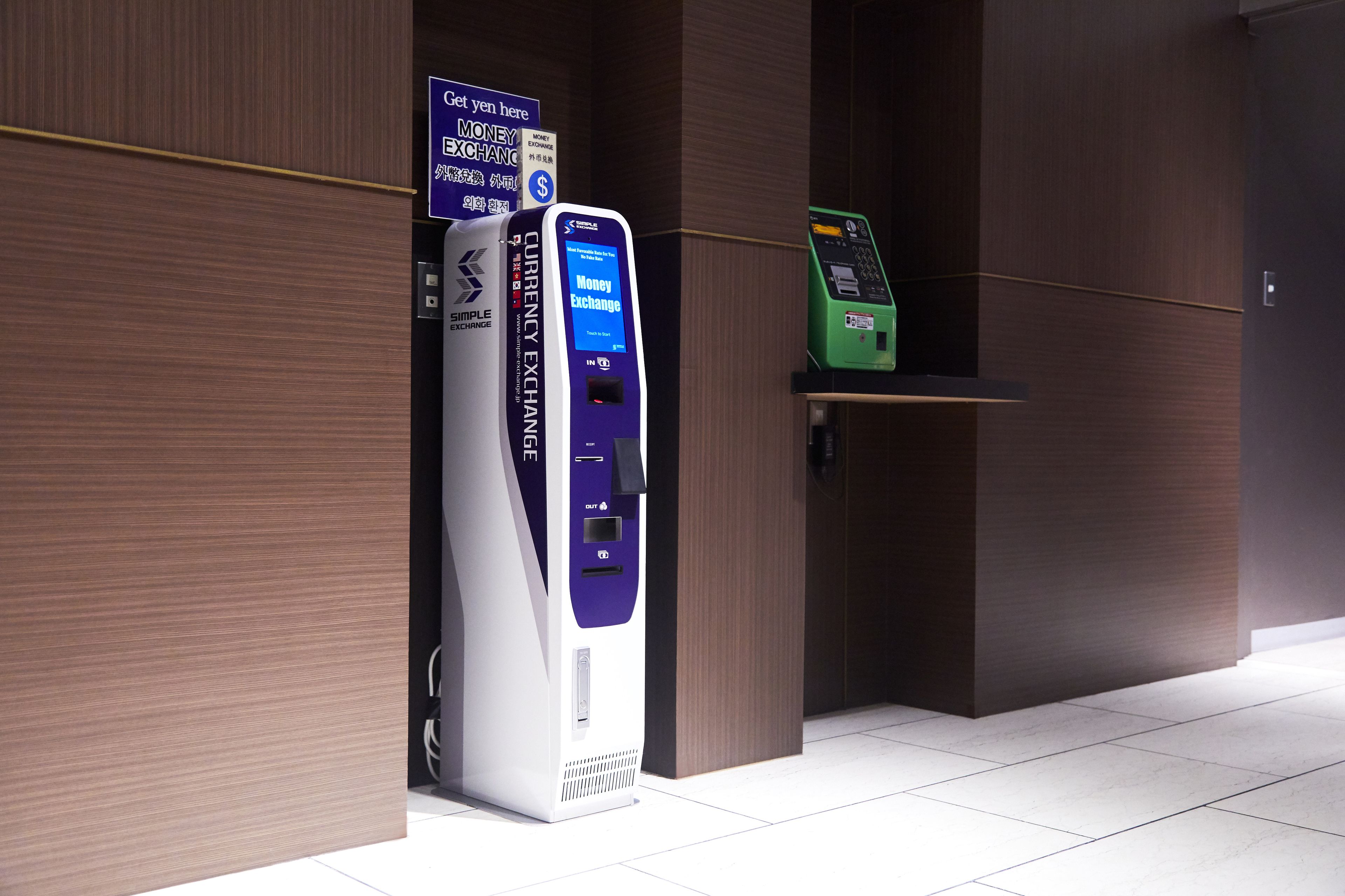 Un cajero de cambio de divisas y un teléfono público verde en un moderno vestíbulo con paneles de madera.