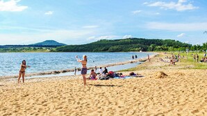 A beach with people sunbathing and playing, a mountain in the background, and a clear sky.