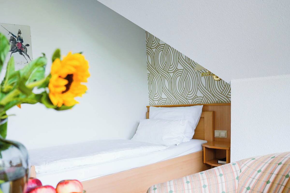 Habitación de hotel con cama, mesita de noche de madera, cabecero estampado, pequeña mesa con fruta y sofá.