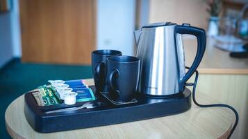 A coffee maker, two black mugs, and a tray with coffee packets on a wooden table.