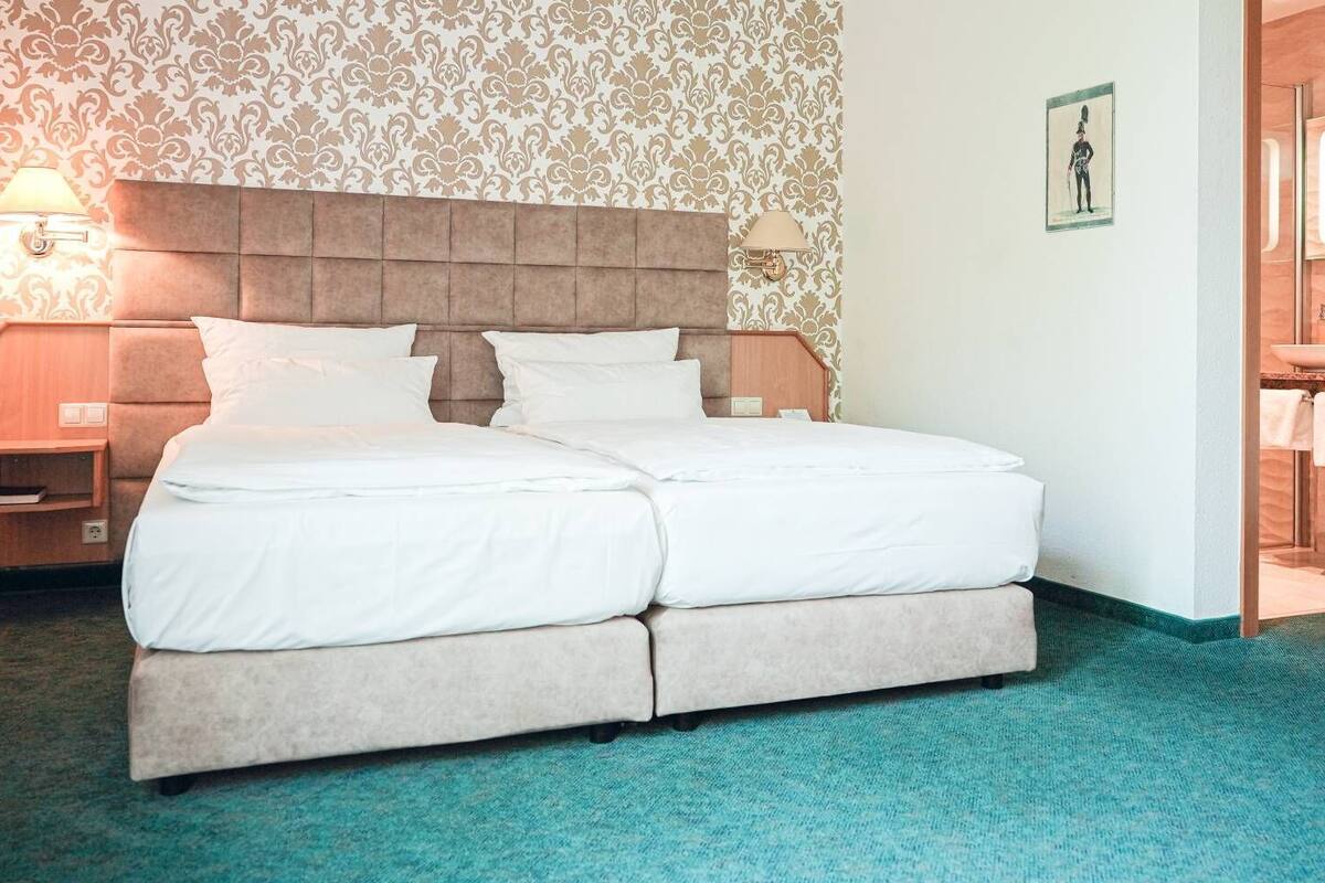 Una cama doble con cabecera, dos mesitas de noche y una pared con papel tapiz estampado.