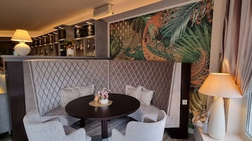Un comedor moderno con una mesa redonda, sillas acolchadas y un centro de mesa decorativo. Se ve un área de bar con estantes llenos de botellas y un menú en una pizarra al fondo.
