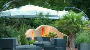 An outdoor seating area with a white umbrella, dark wicker furniture, and a palm tree.