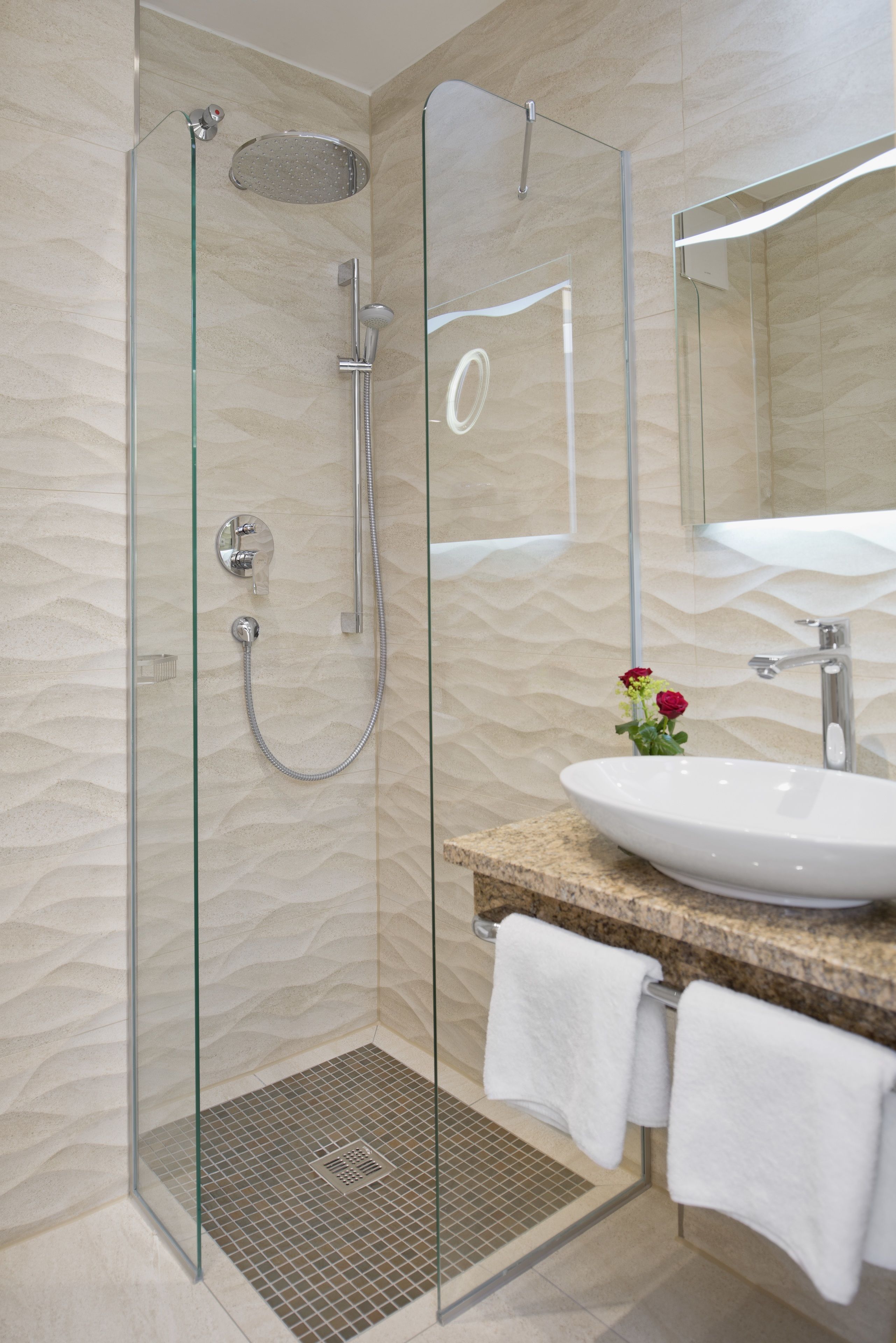 A modern bathroom with a glass-enclosed shower, a sink with a marble countertop, and a mirror above the sink.