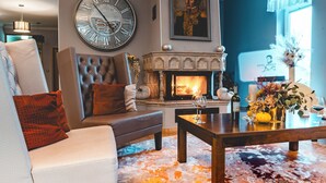 A living room with a fireplace, a large wall clock, and a portrait.