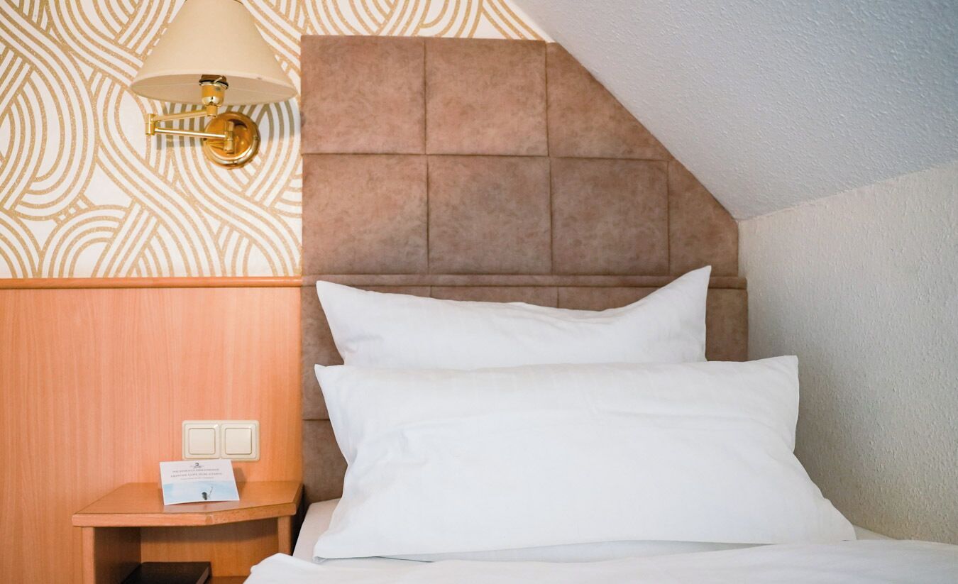 A hotel room with a wooden headboard, a bedside table with a lamp, and a sign indicating room amenities.