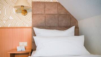A hotel room with a wooden headboard, a bedside table with a lamp, and a sign indicating room amenities.