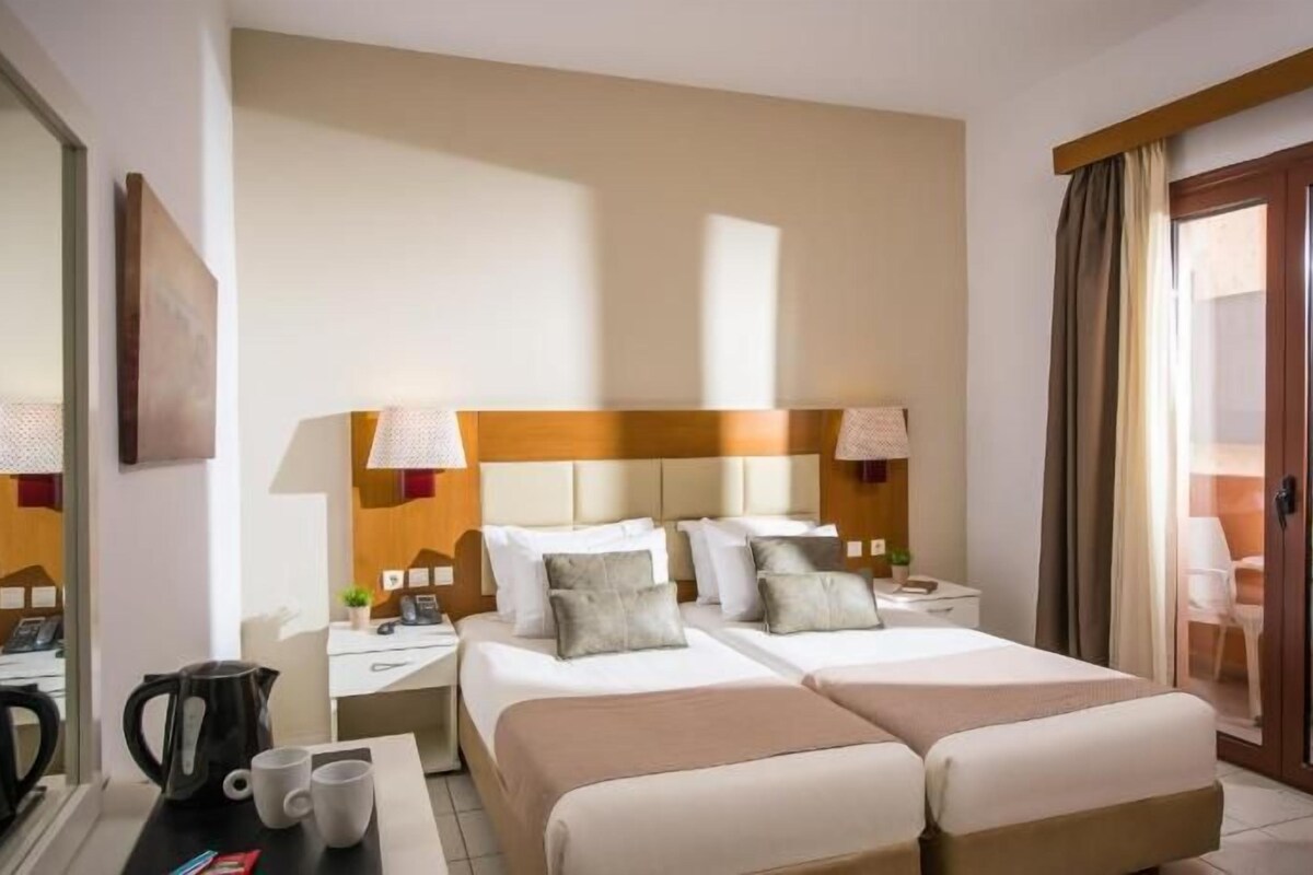 A hotel room with two beds, a desk, a chair, a coffee maker, and a balcony with a view.