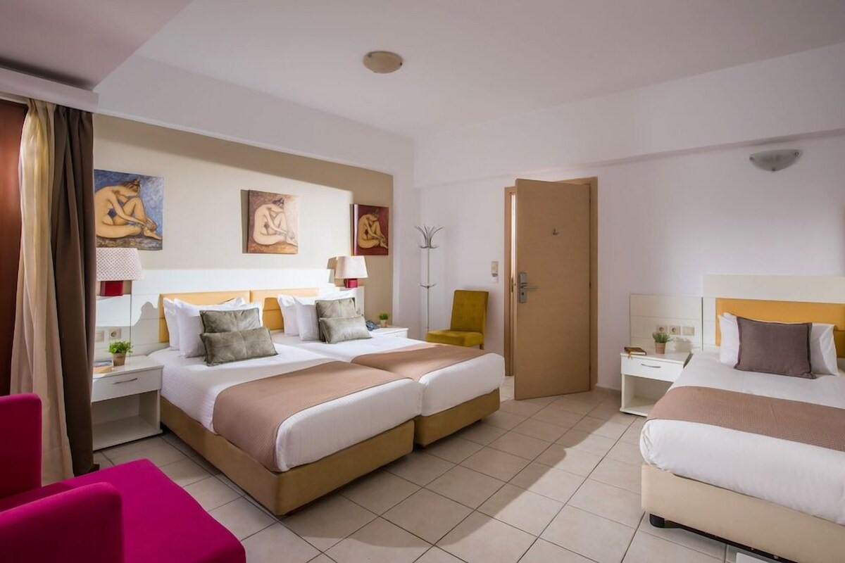 A hotel room with two beds, a desk, a chair, and artwork on the walls.