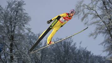 A skier in a yellow suit mid-air, with trees in the background.