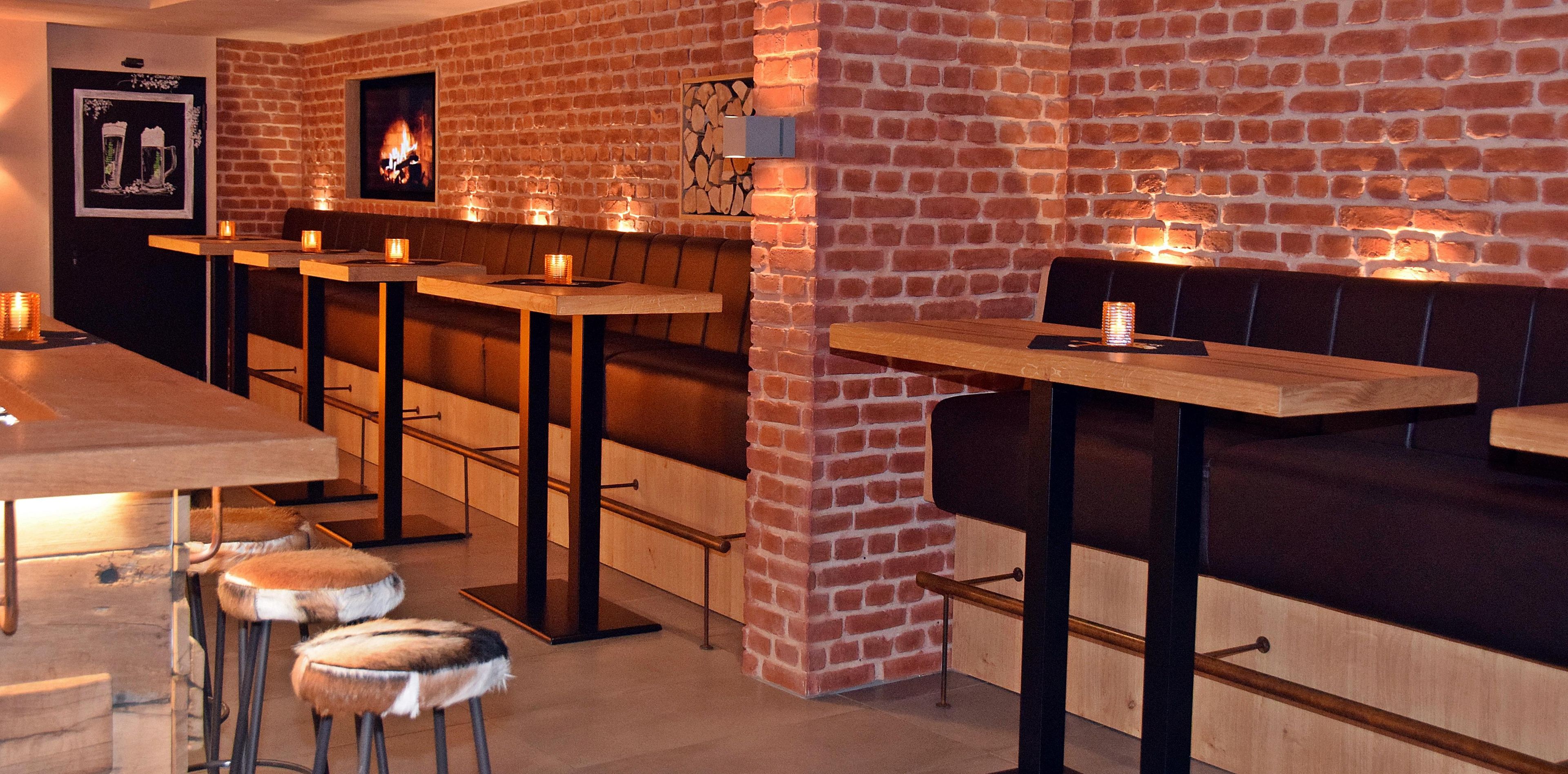 A bar area with brick walls, wooden stools, and tables.