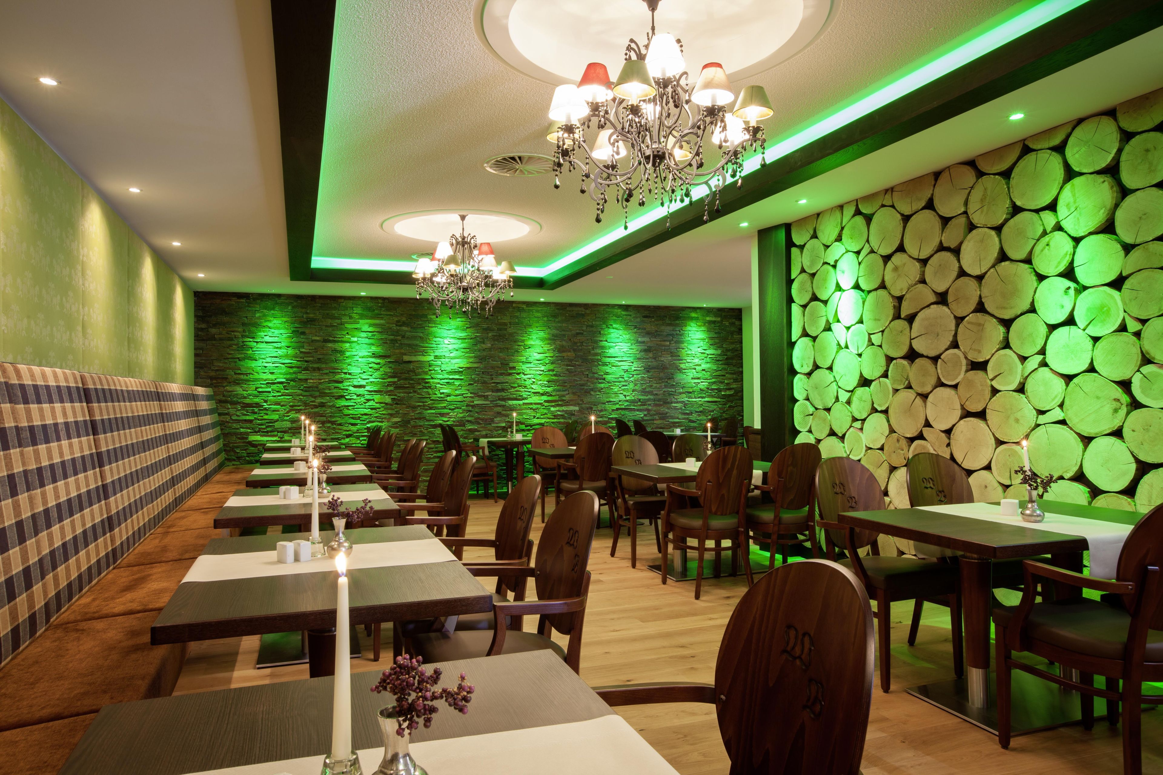 A restaurant interior with a green-lit wall, wooden tables, and chairs.