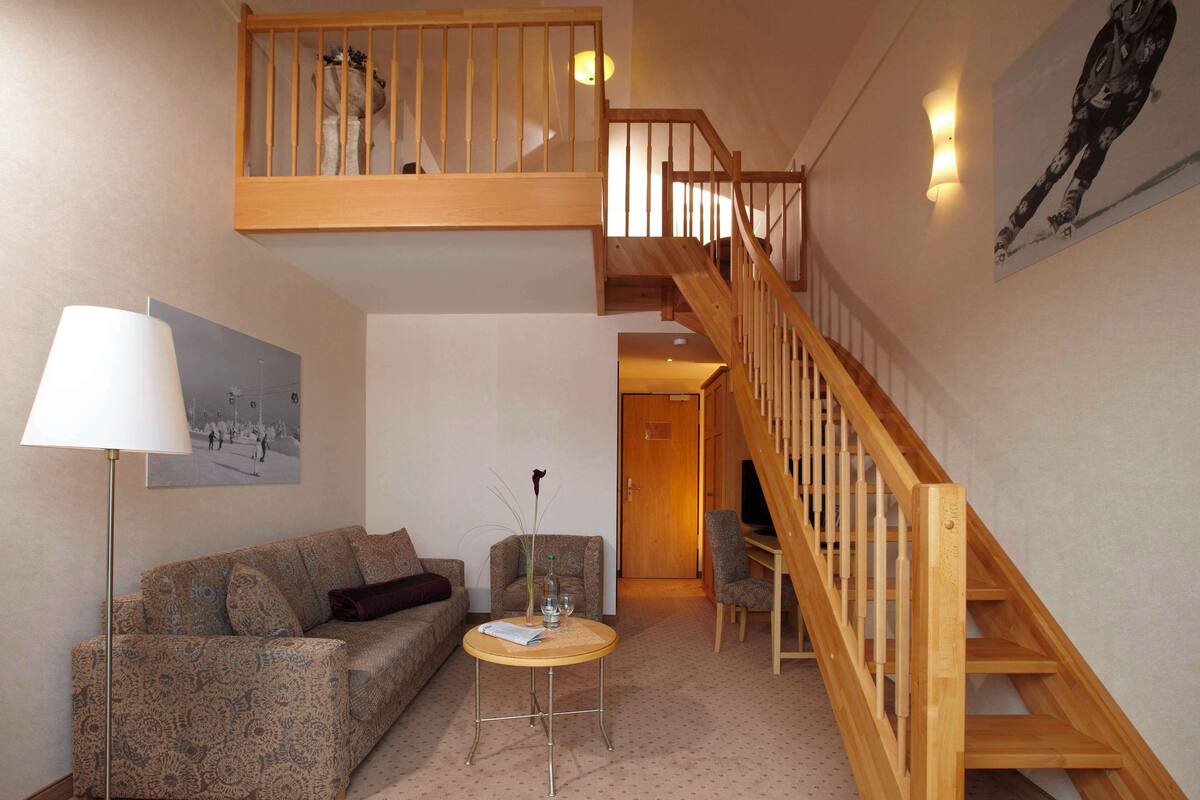 Un salon avec un canapé, une petite table ronde, une lampe, un tableau et un escalier en bois.