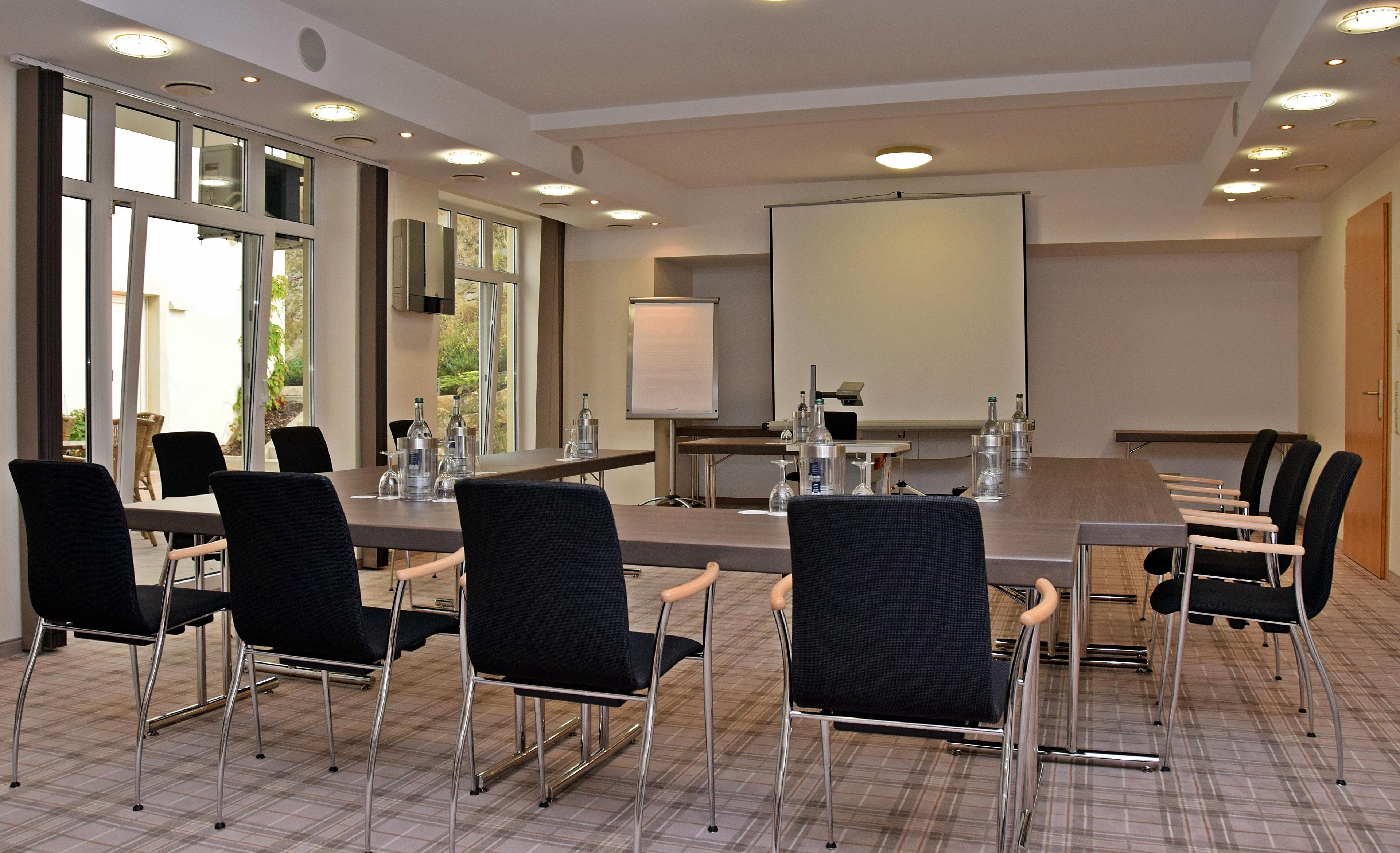 Ein Konferenzraum mit einem langen Tisch, Stühlen, einer Projektionsleinwand und einer Whiteboard-Tafel.