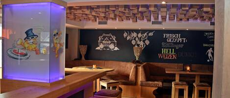 A bar area with wooden stools, a bar counter, and a wall with decorative elements and text.