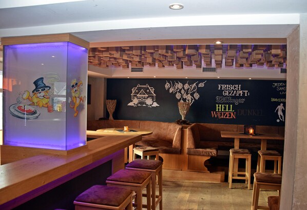 A bar area with wooden stools, a bar counter, and a wall with decorative elements and text.