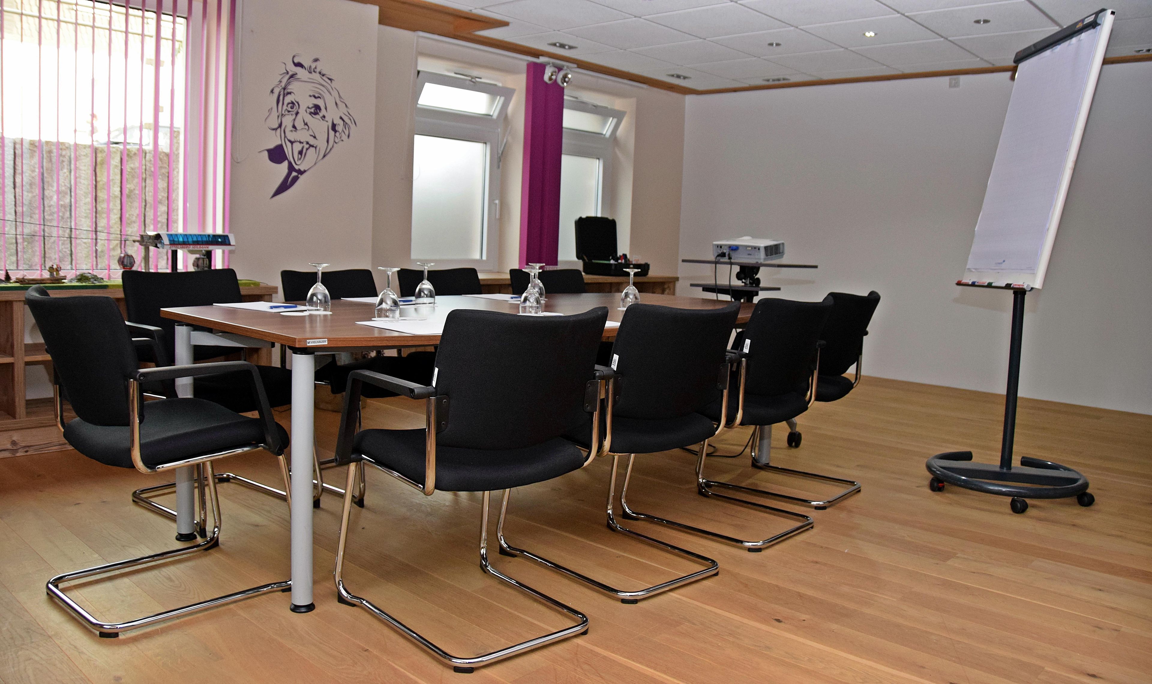 A conference room with a wooden table, black chairs, a whiteboard, and a projector.