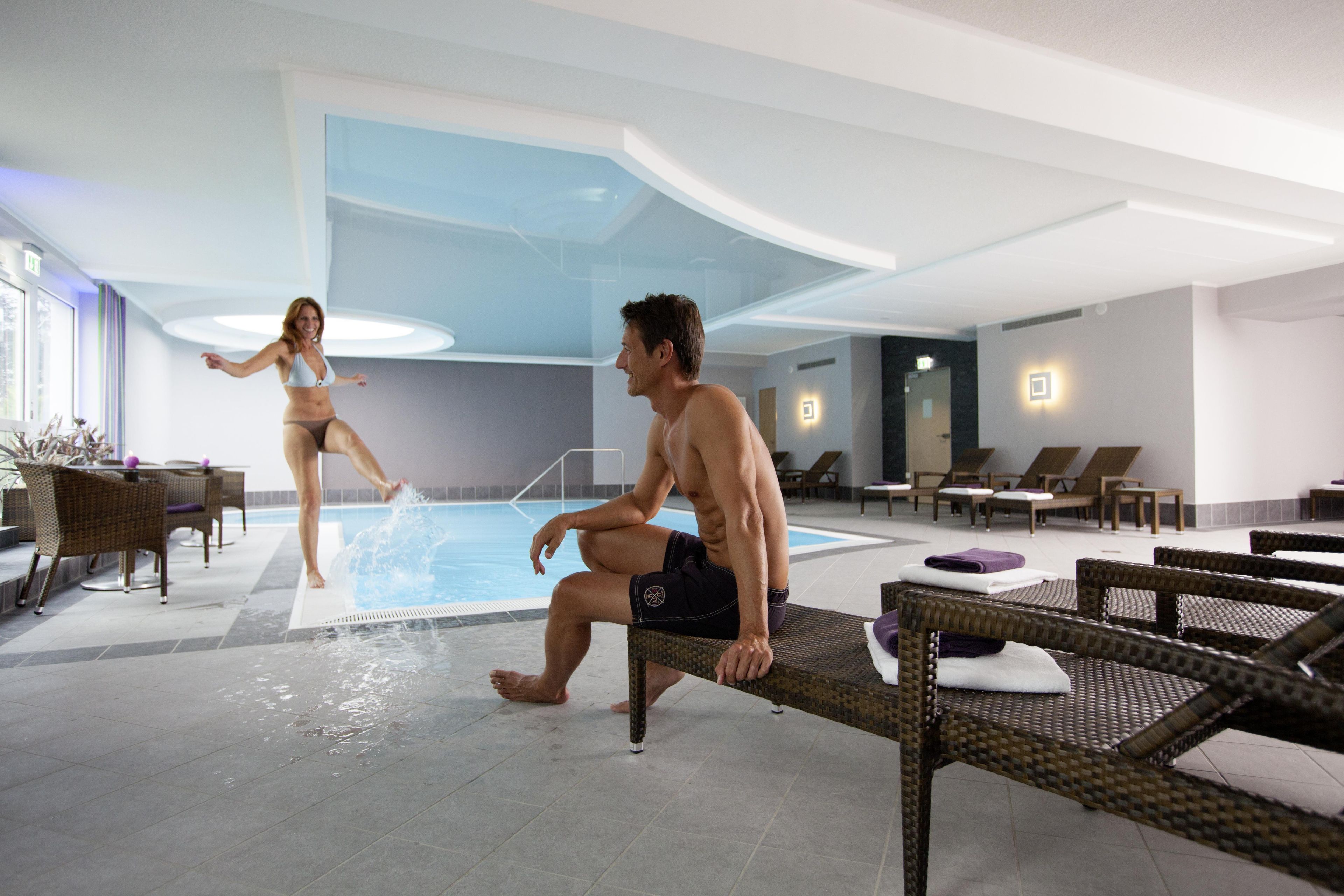 Zona de piscina con sillones de descanso y una pareja junto a la piscina.