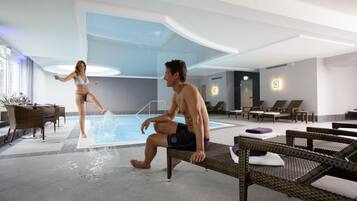 Zona de piscina con sillones de descanso y una pareja junto a la piscina.